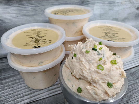 Containers of creamy smoked halibut dip topped with green onions on a rustic wooden surface.