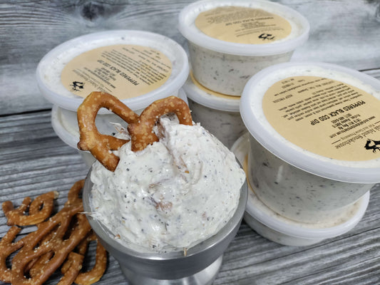 Containers of creamy smoked black cod dip with visible black pepper and sesame seeds on a rustic wood surface.