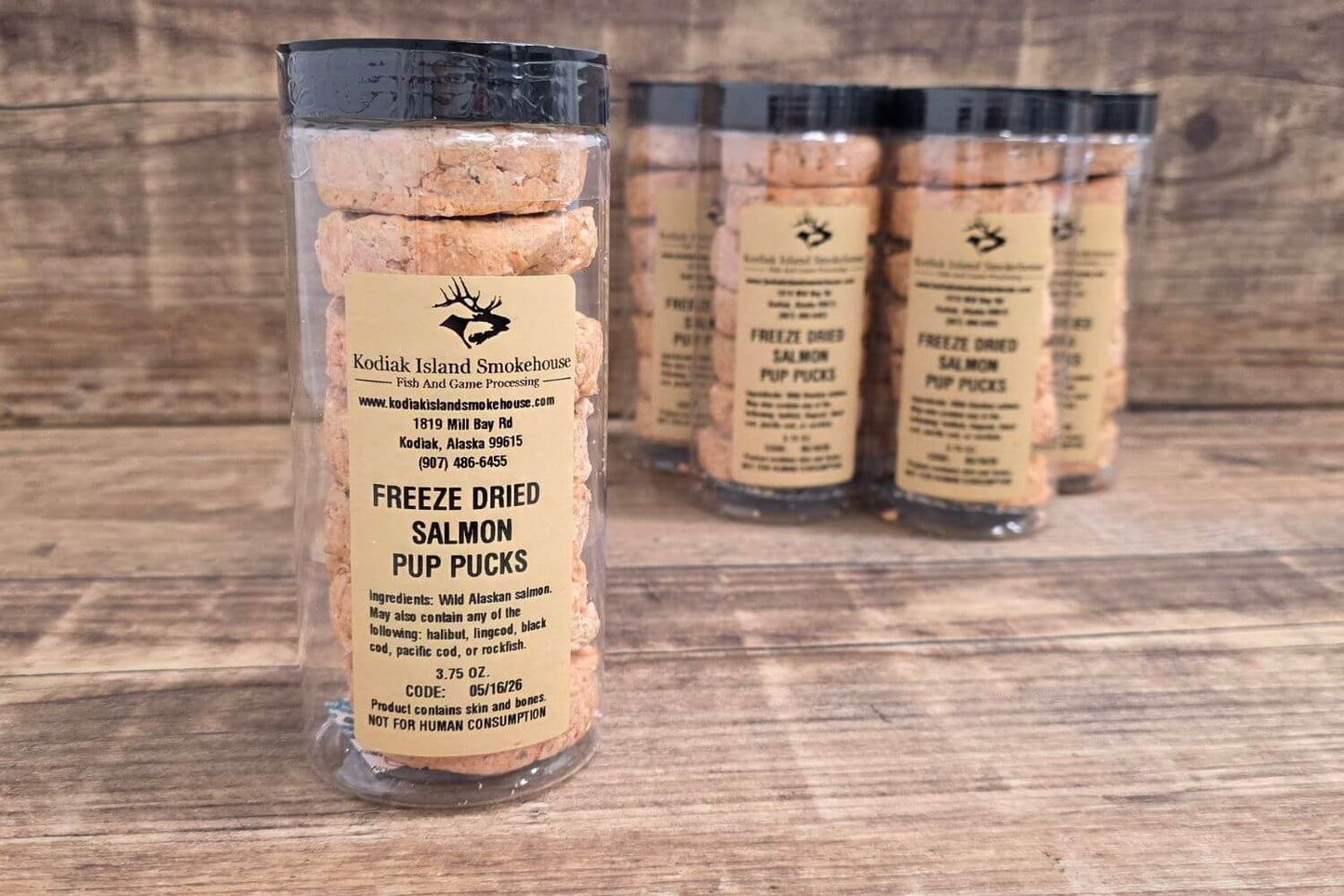 Freeze-dried salmon pup pucks packaged in clear tubes on a rustic wooden surface.