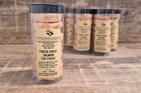 Freeze-dried salmon pup pucks packaged in clear tubes on a rustic wooden surface.