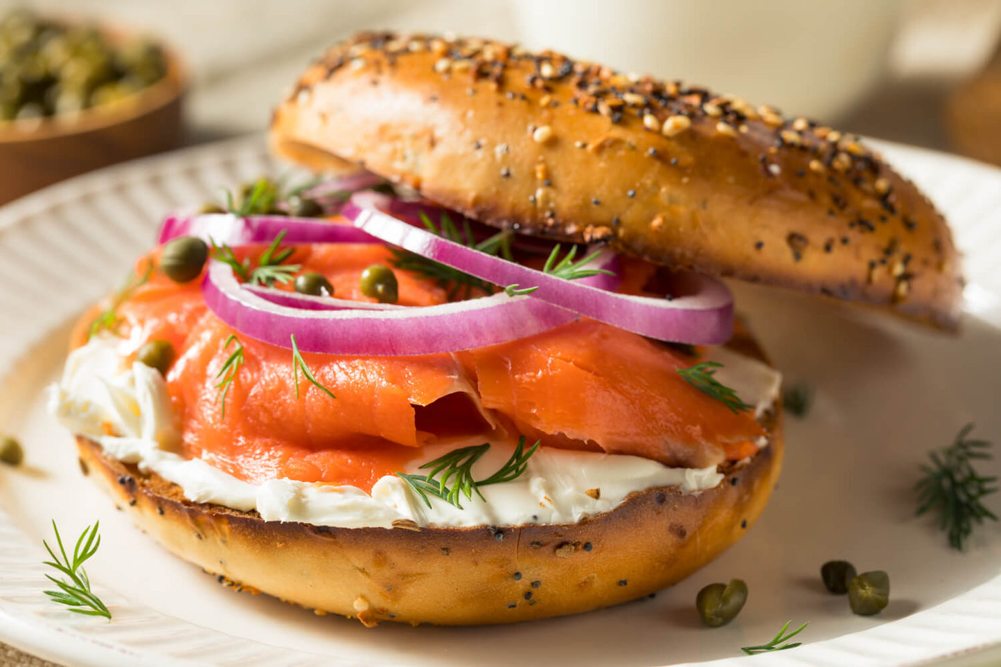 Bagel with salmon gravlax, cream cheese, and onions on a white plate.