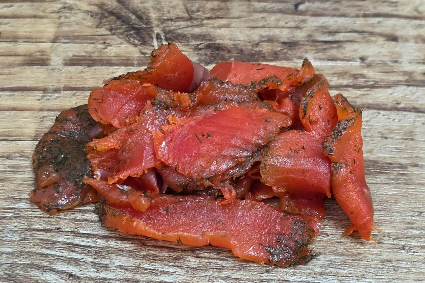 Slices of dill cured wild Alaskan salmon gravlax on a rustic wooden board.