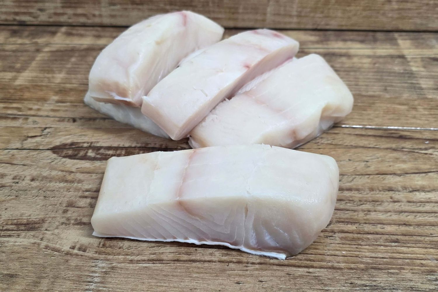 Raw Alaskan halibut portions arranged on a rustic wooden surface.
