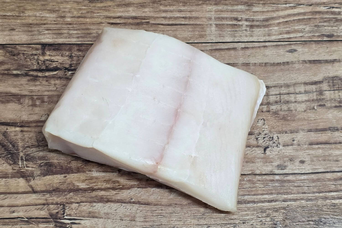 Raw Wild Alaskan halibut portion showing the natural grain and ivory color on a rustic wood background.