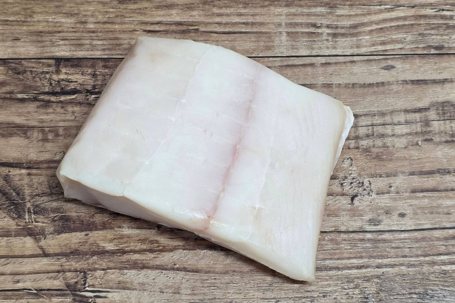 Raw Wild Alaskan halibut portion showing the natural grain and ivory color on a rustic wood background.