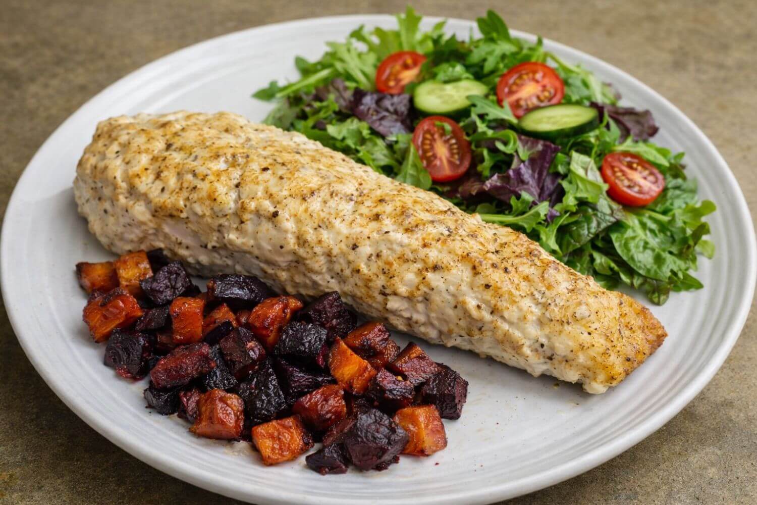 Plated dish with roasted vegetables, Olympia inspired halibut, and a side salad on a white plate.