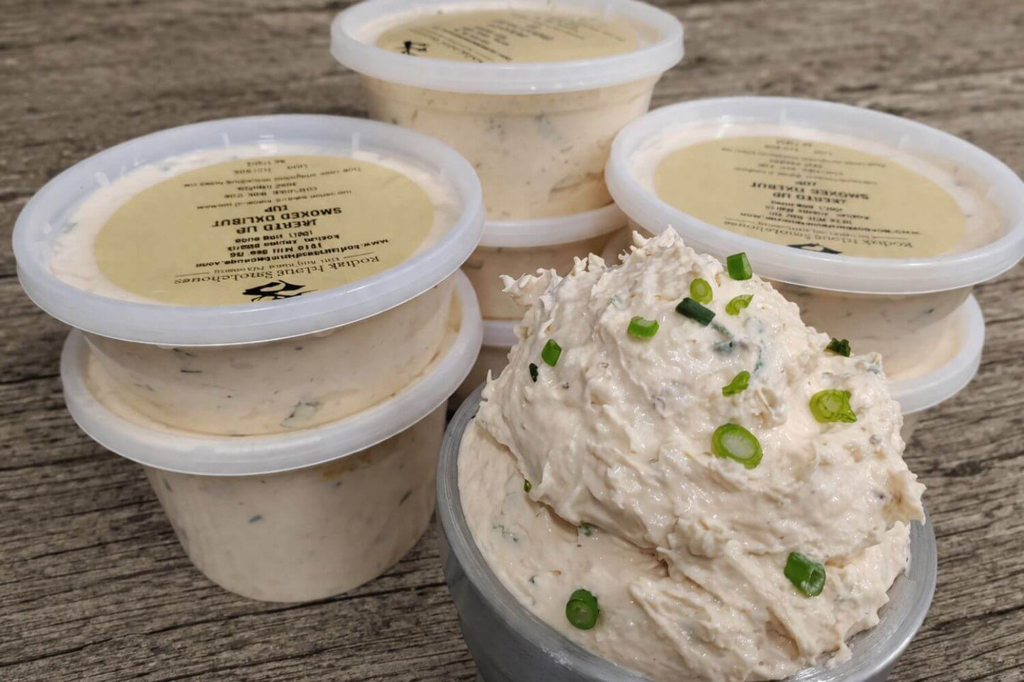 Containers of creamy smoked halibut dip topped with green onions on a rustic wooden surface.