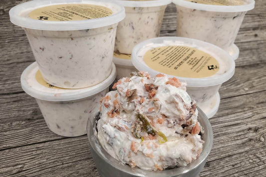 Containers of jalapeño smoked salmon dip with visible smoked salmon flakes and jalapeño pieces on a rustic wood surface.