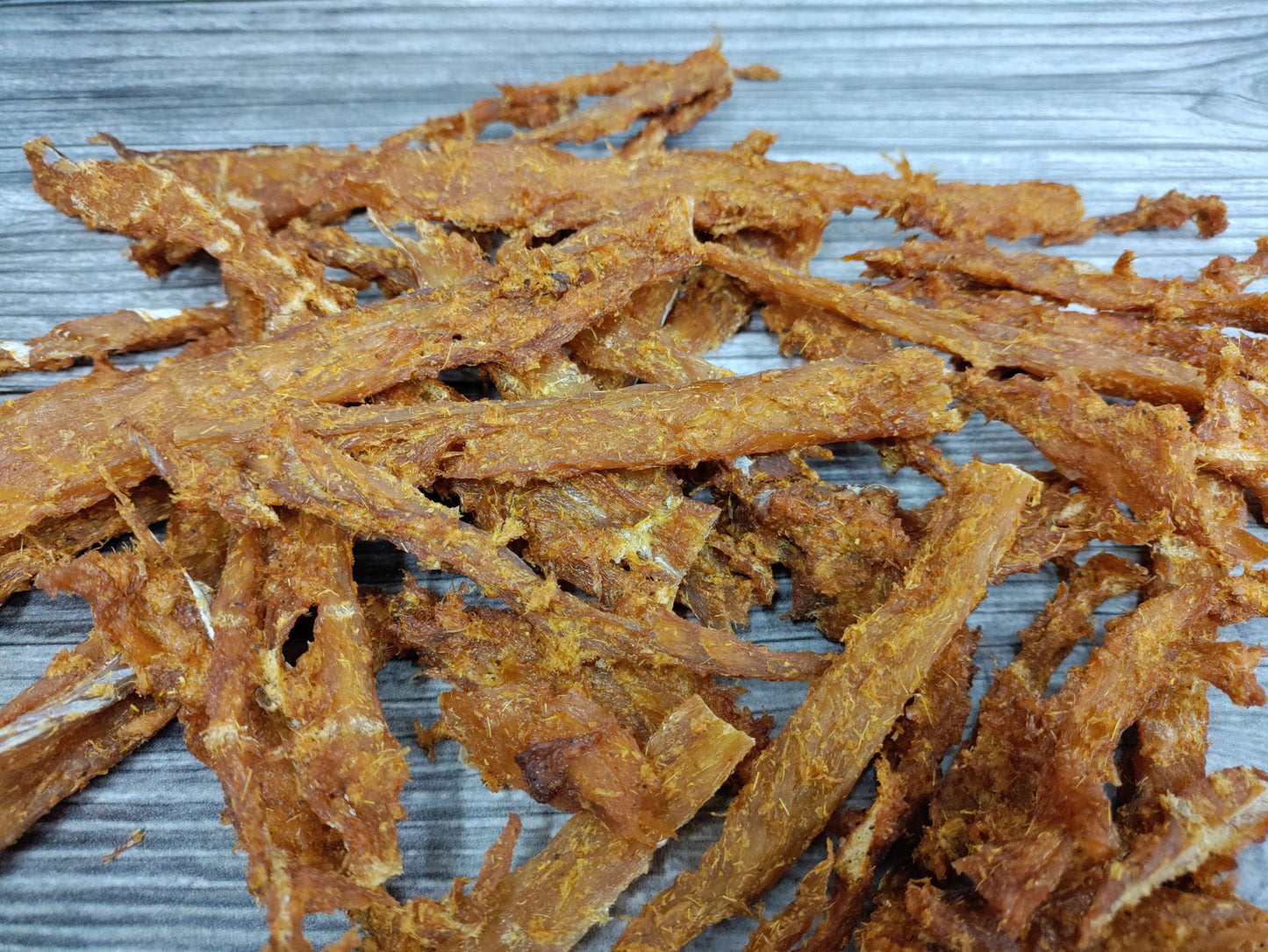 Smoked curry-seasoned wild cod jerky pieces on a wooden board.
