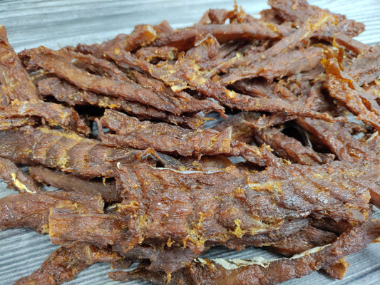 Sweet teriyaki-seasoned wild cod jerky strips on a wooden board.