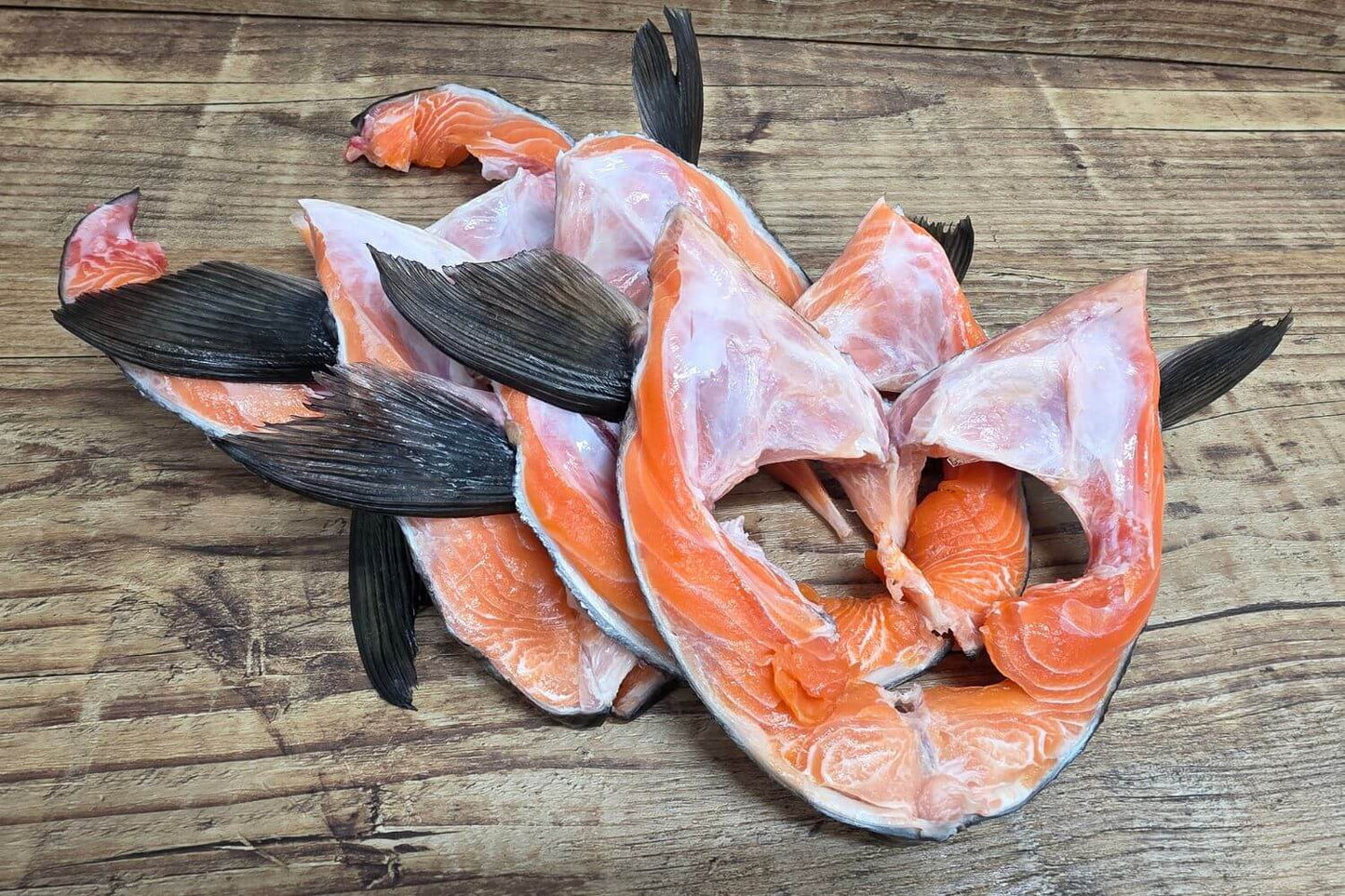 Raw wild Alaskan King Salmon collars arranged on a rustic wooden surface, showing rich orange flesh and natural marbling.