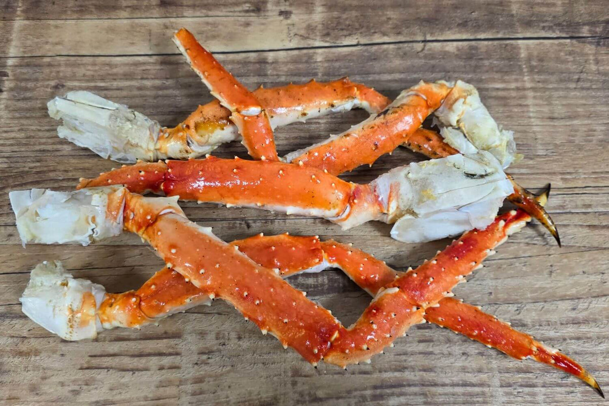 Several Wild Alaskan red king crab leg clusters displayed on a rustic wood surface