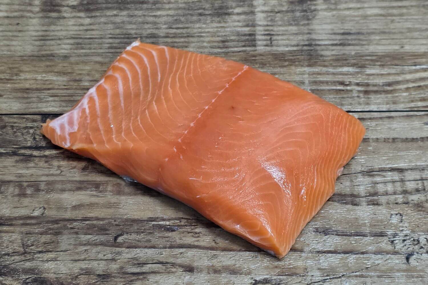 Raw Wild Alaskan king salmon portion showing bright orange color and clean marbling on rustic wood.