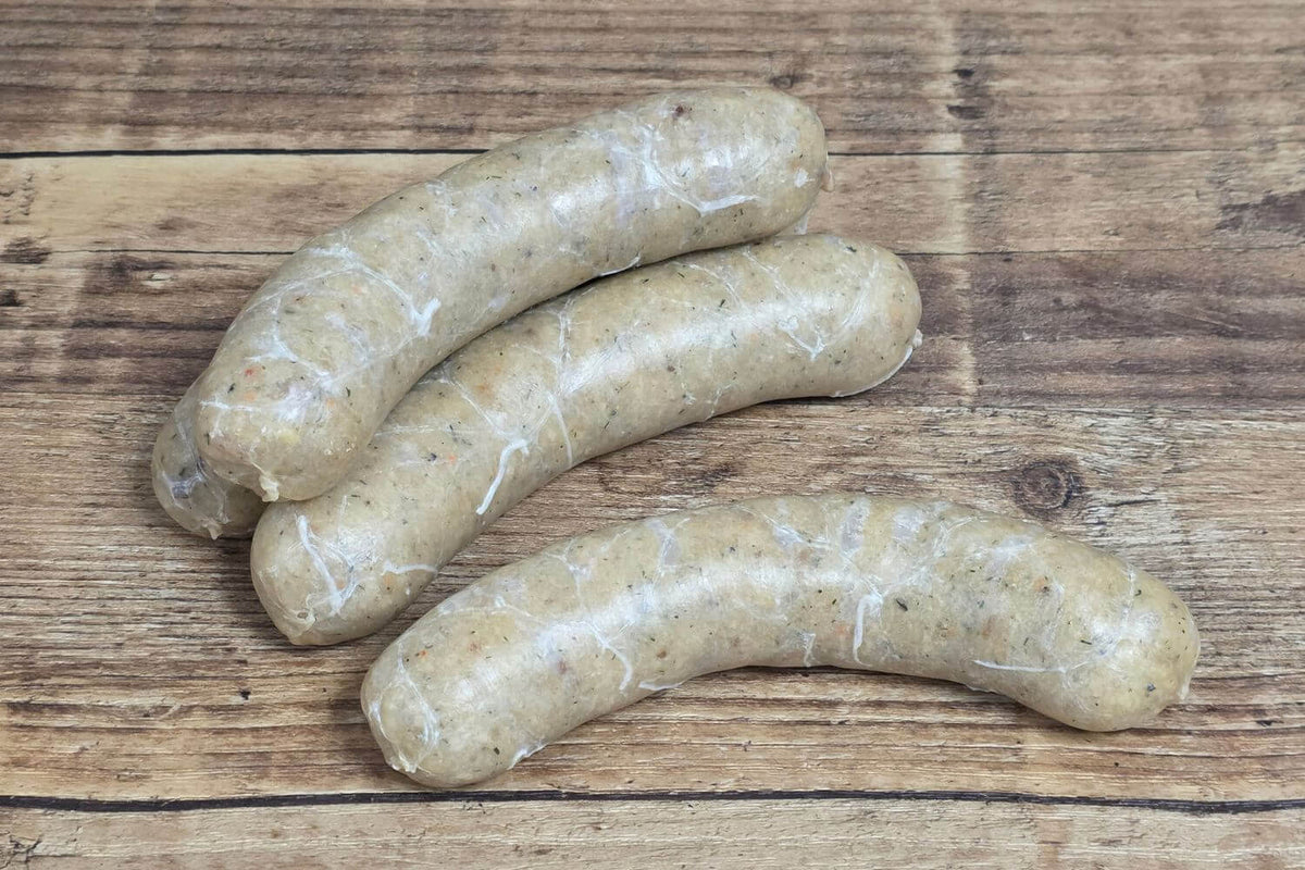 Three raw wild Alaskan lingcod whitefish sausage links in natural hog casings, arranged on a rustic wooden surface.