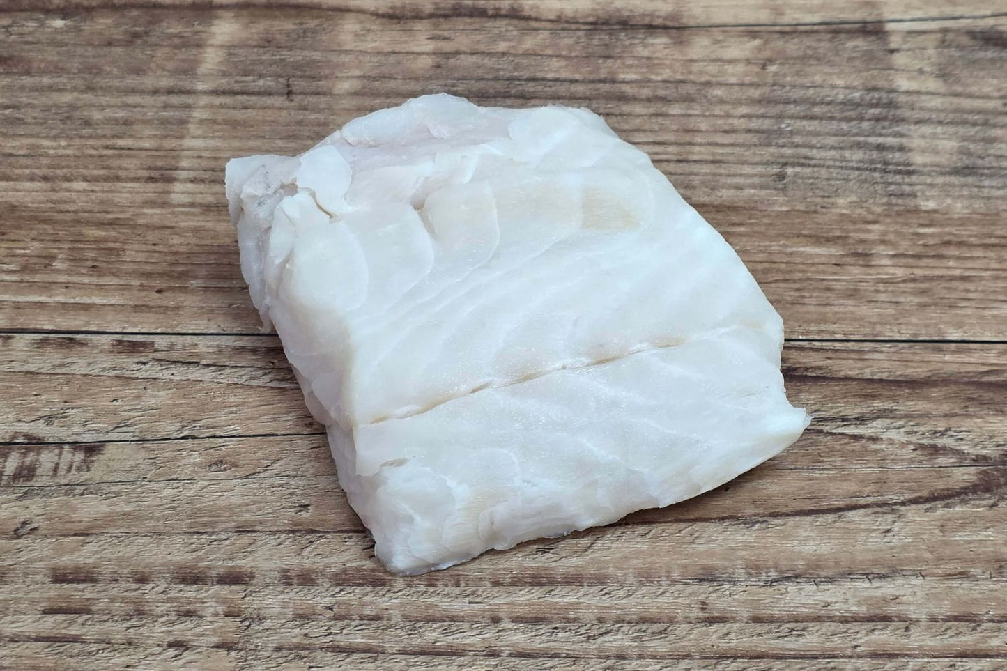 Wild Alaskan lingcod portion displayed on a rustic wood table, highlighting its firm Kodiak-caught white flesh.
