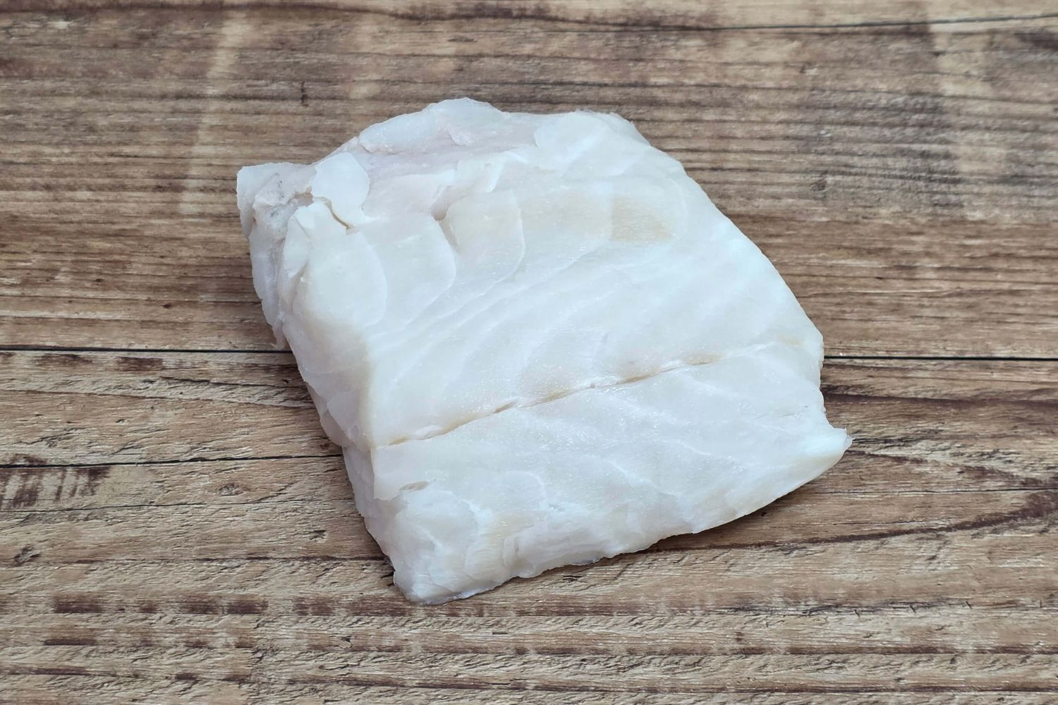 Wild Alaskan lingcod portion displayed on a rustic wood table, highlighting its firm Kodiak-caught white flesh.
