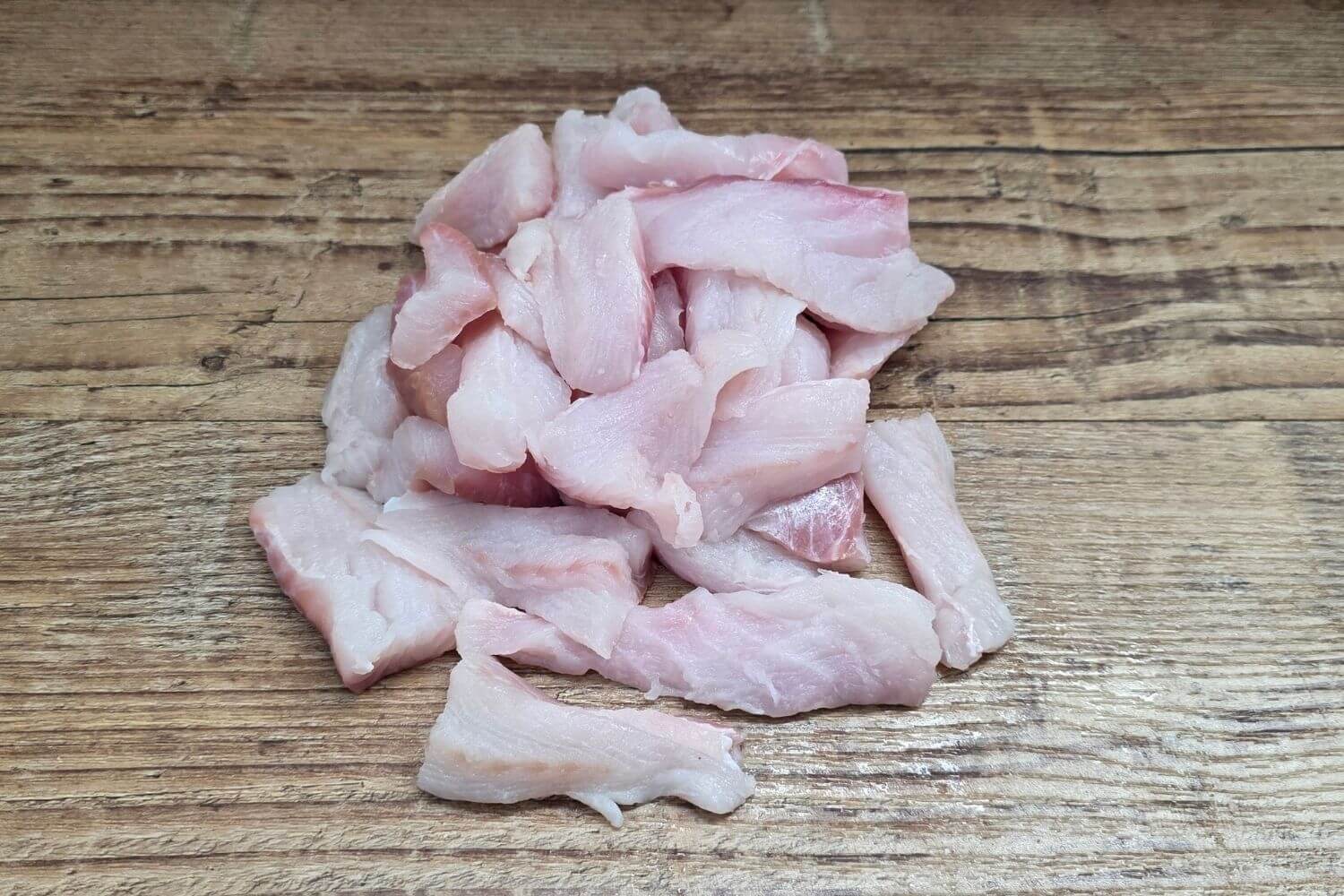 Wild Alaskan lingcod Ready Cuts in naturally varied strips and pieces on a rustic wooden surface.
