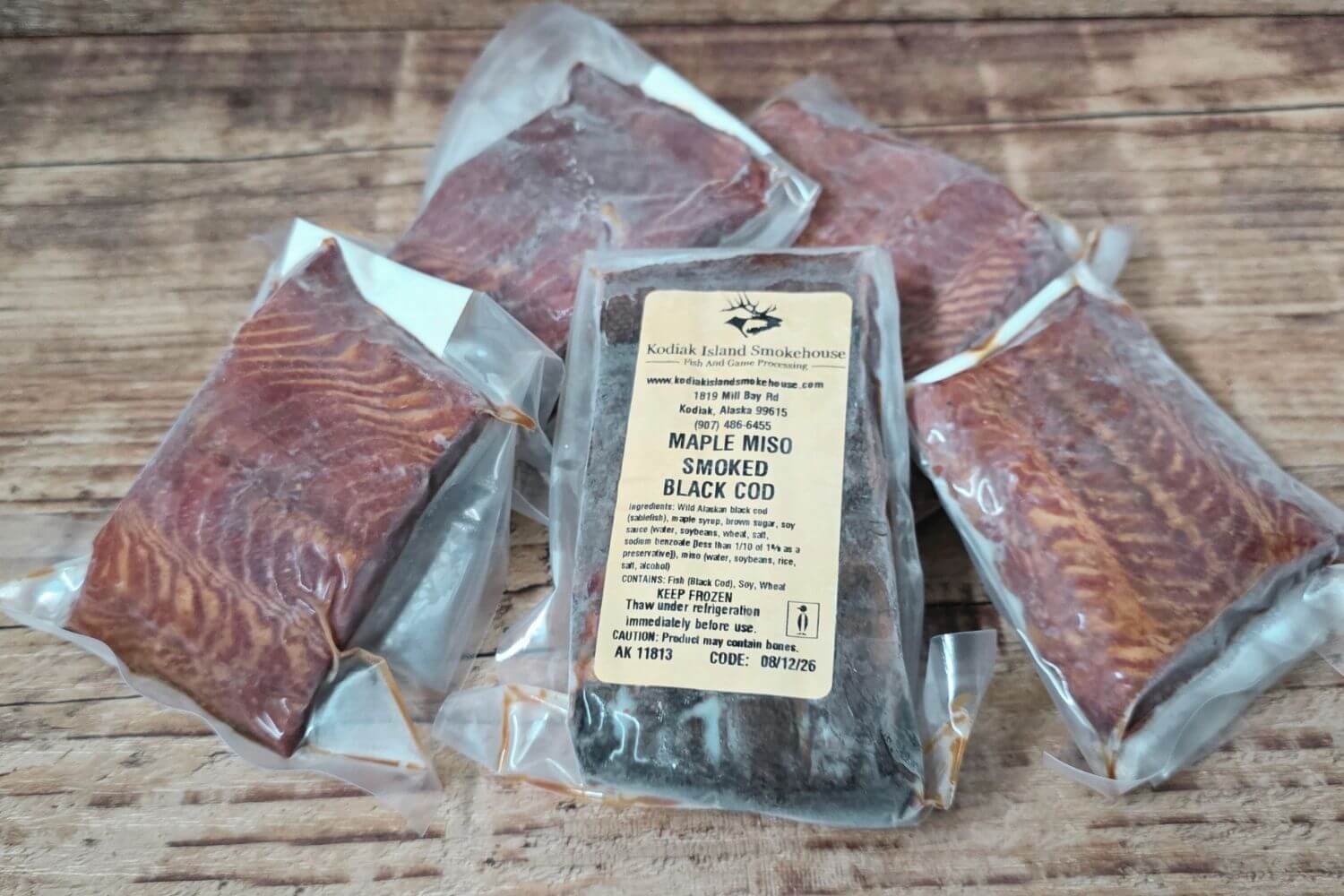 Vacuum-sealed packages of Maple Miso Smoked Black Cod from Kodiak Island Smokehouse displayed on a rustic wooden surface.