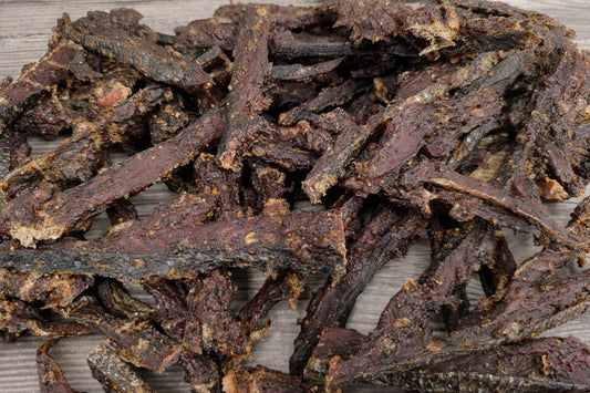 Smoked wild sockeye pepper jerky strips piled on a wooden board.