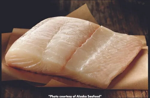 Raw halibut portion on parchment paper on a wooden surface.