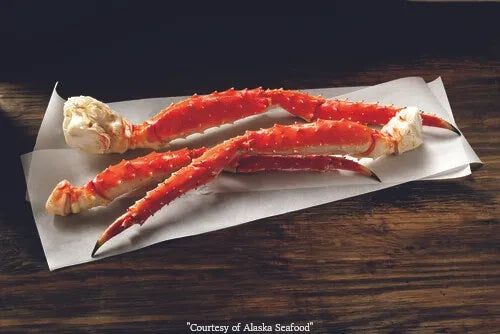 Red King Crab leg clusters on parchment, vibrant red shell with natural texture.