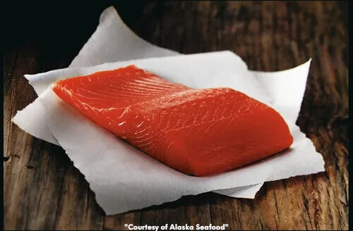 Sushi-grade sockeye salmon portion on parchment over rustic wood.