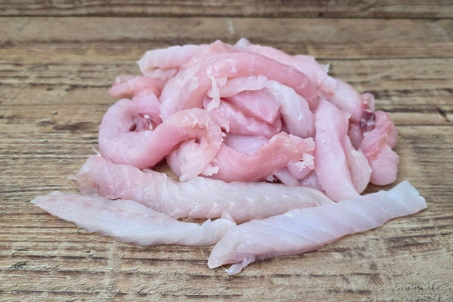 Wild Alaska rockfish ready cuts in naturally varied strips and pieces on a rustic wooden surface.