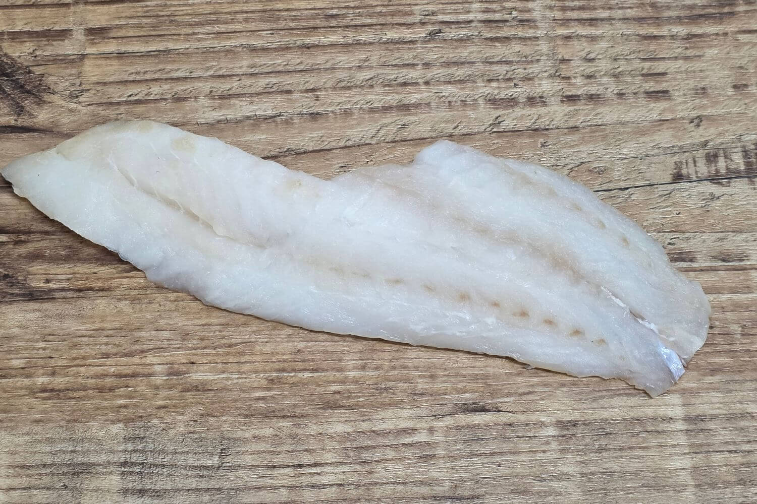 Skinless rockfish fillet on rustic wood surface.