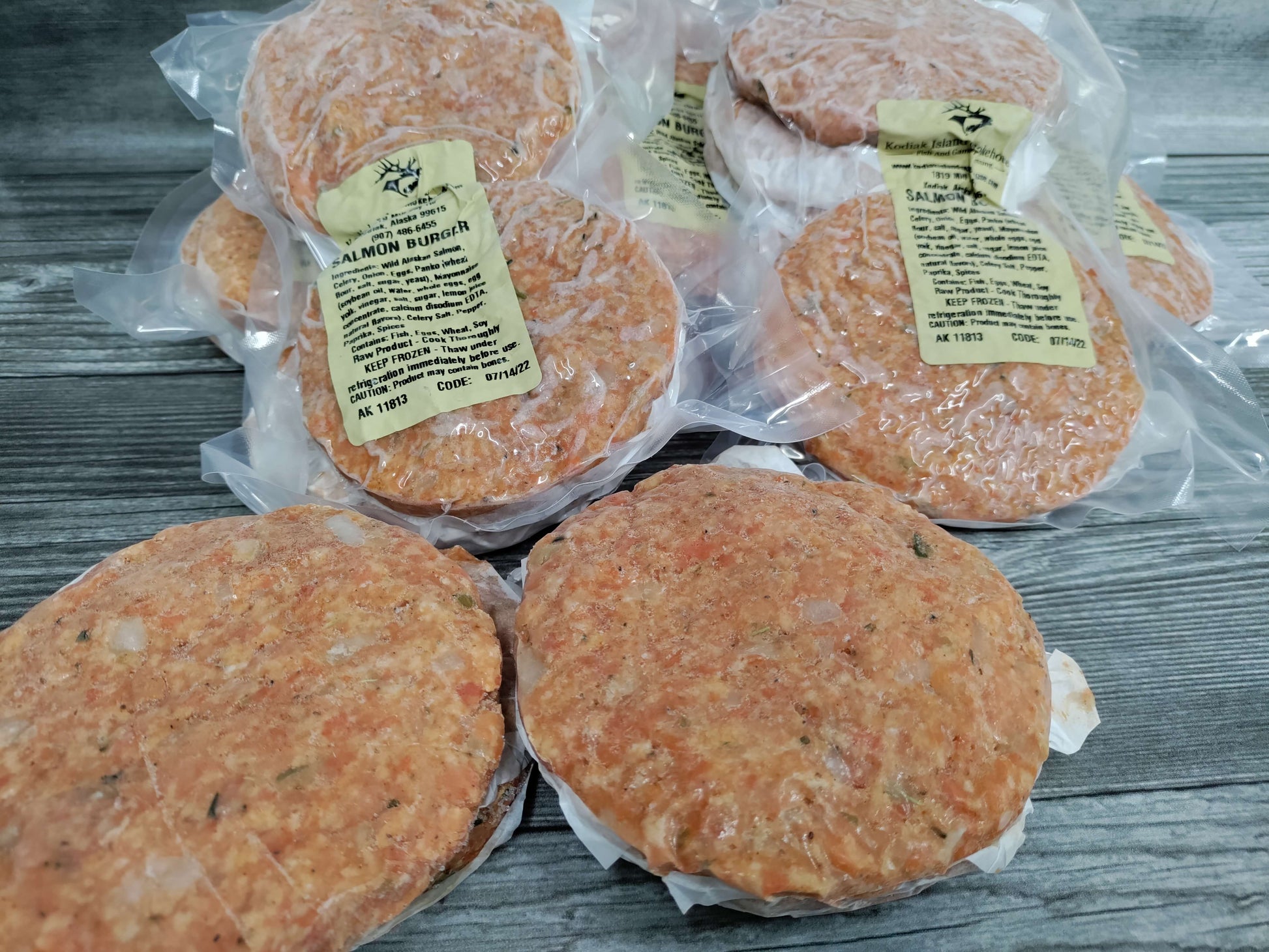 Vacuum sealed wild Alaskan salmon burger patties arranged on a rustic wooden surface.