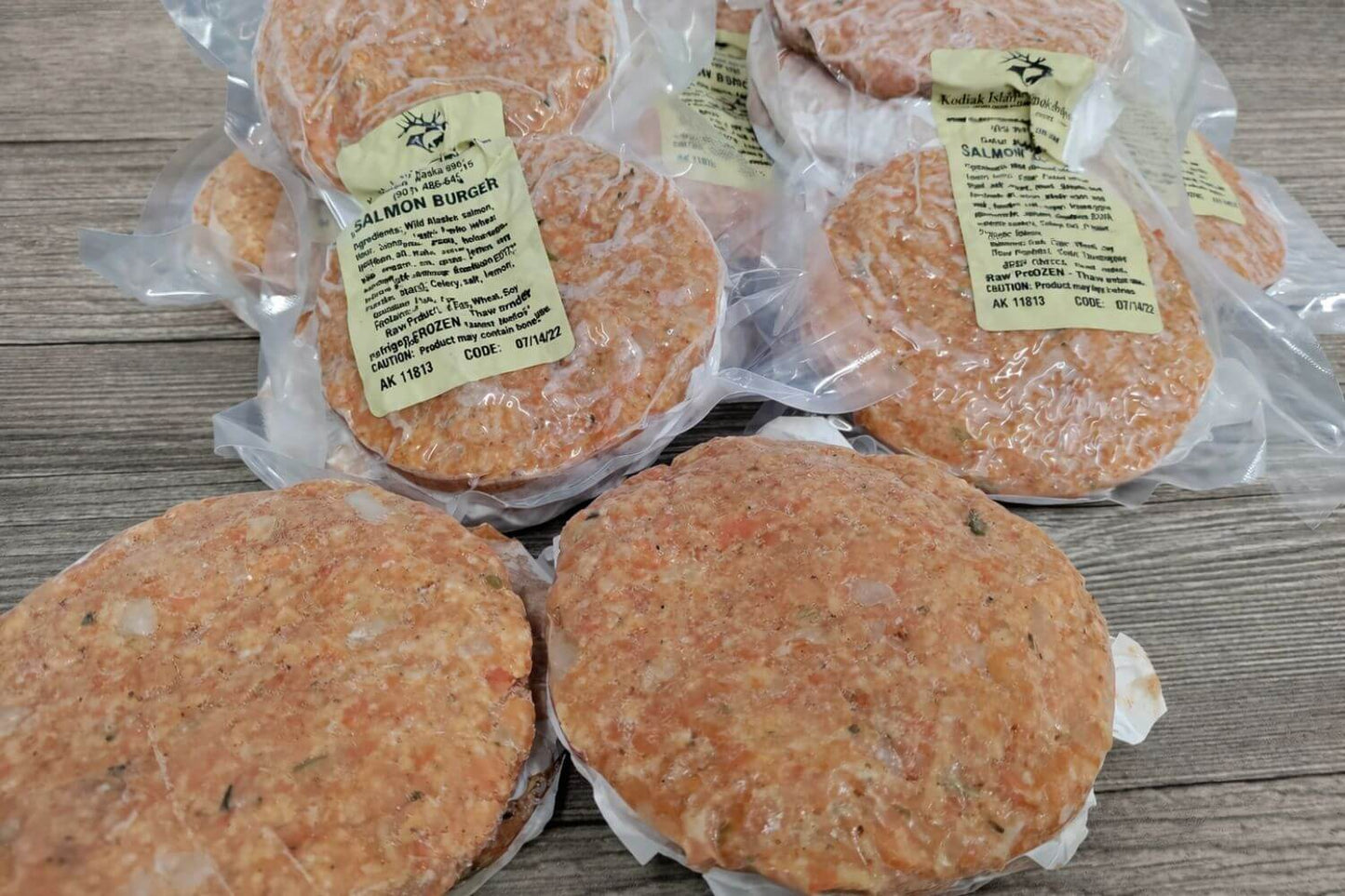 Vacuum sealed wild Alaskan salmon burger patties arranged on a rustic wooden surface.