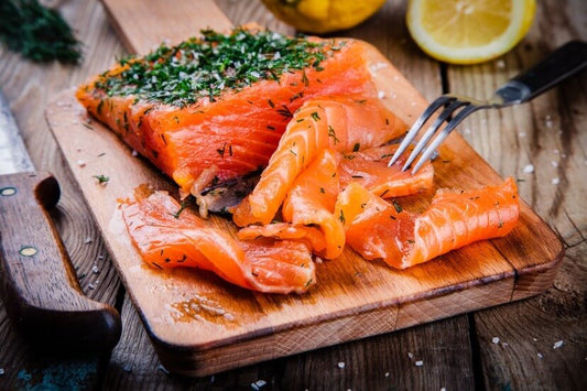 Slices of dill cured wild Alaskan salmon gravlax on a wooden board with citrus and herbs.