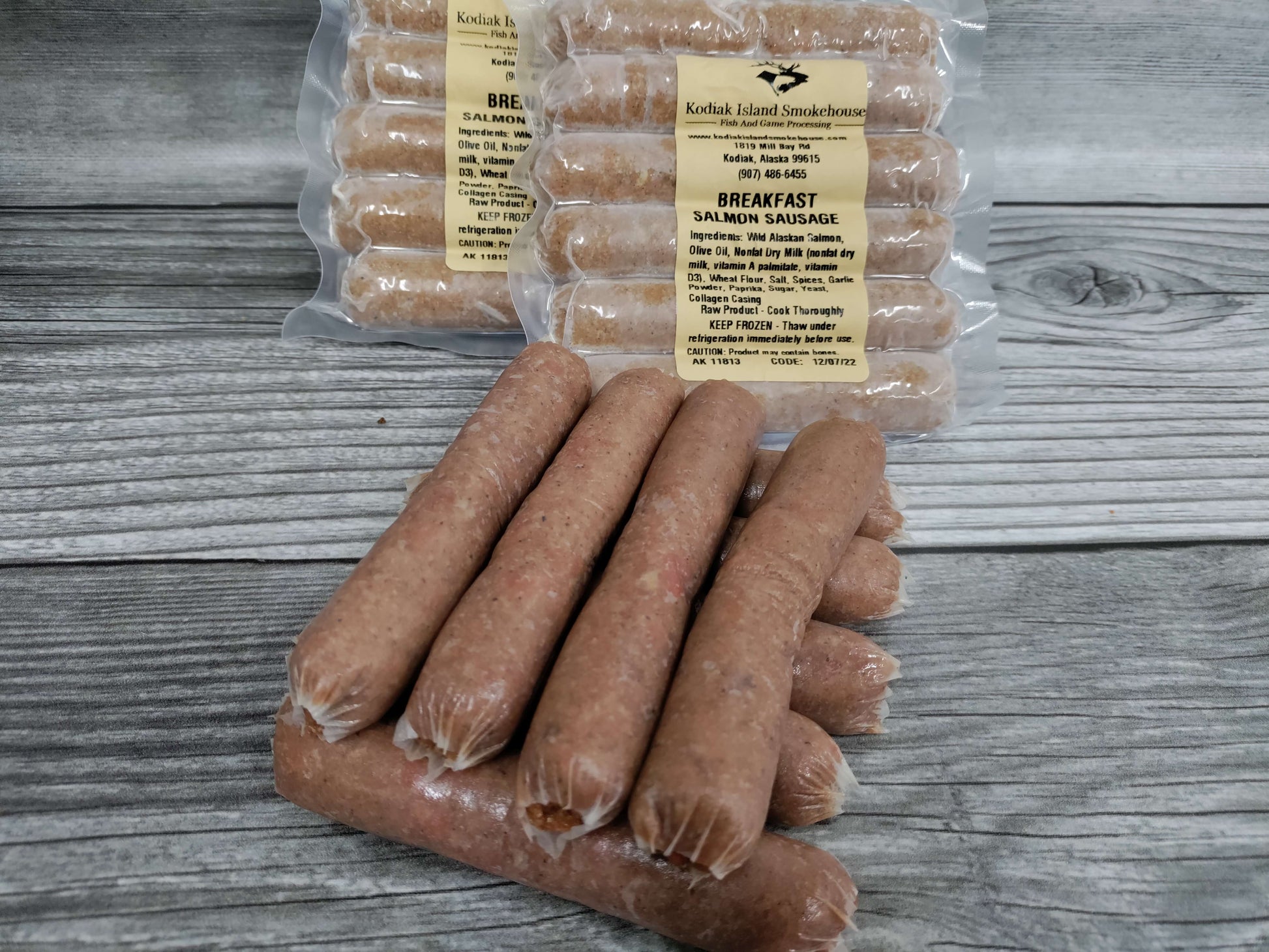 Vacuum-sealed packages of wild Alaskan salmon breakfast sausage links on a rustic wood surface.