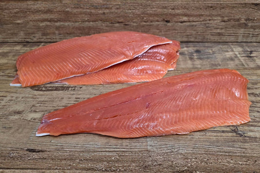 Raw Wild Alaskan coho salmon fillets laid out on a rustic wood surface, showing their bright red-orange color and clean trim.