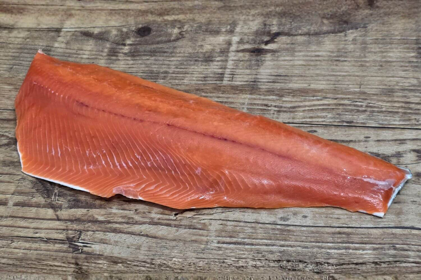 Full raw Wild Alaskan coho salmon fillet displayed on a rustic wooden background, showing its bright orange-red color, smooth grain, and natural sheen.