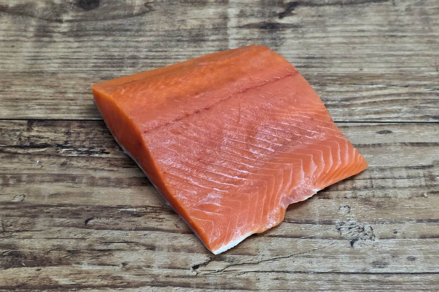 Raw Wild Alaskan coho salmon fillet portion on a rustic wood surface.