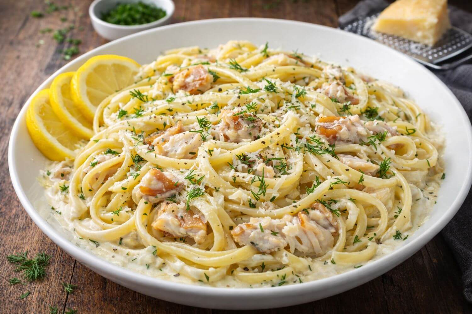 Platter of pasta with smoked black cod, lemon slices and herbs on a wooden table