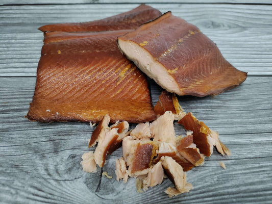 Portions and flakes of smoked wild Alaskan keta salmon on a wooden board.