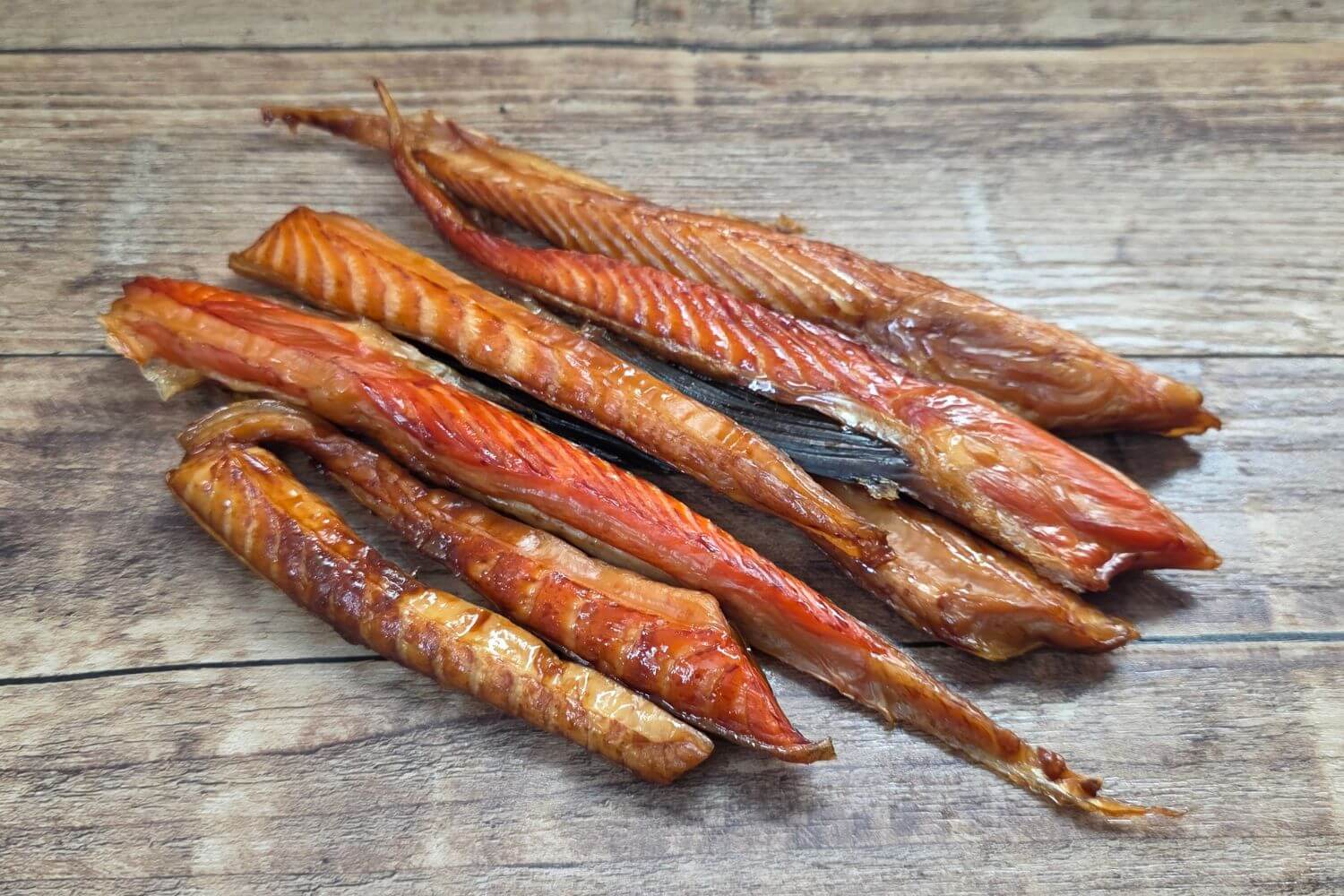 Smoked King Salmon Bellies on wooden background. Made from wild Alaskan king salmon, showing rich smoked flesh and natural marbling.
