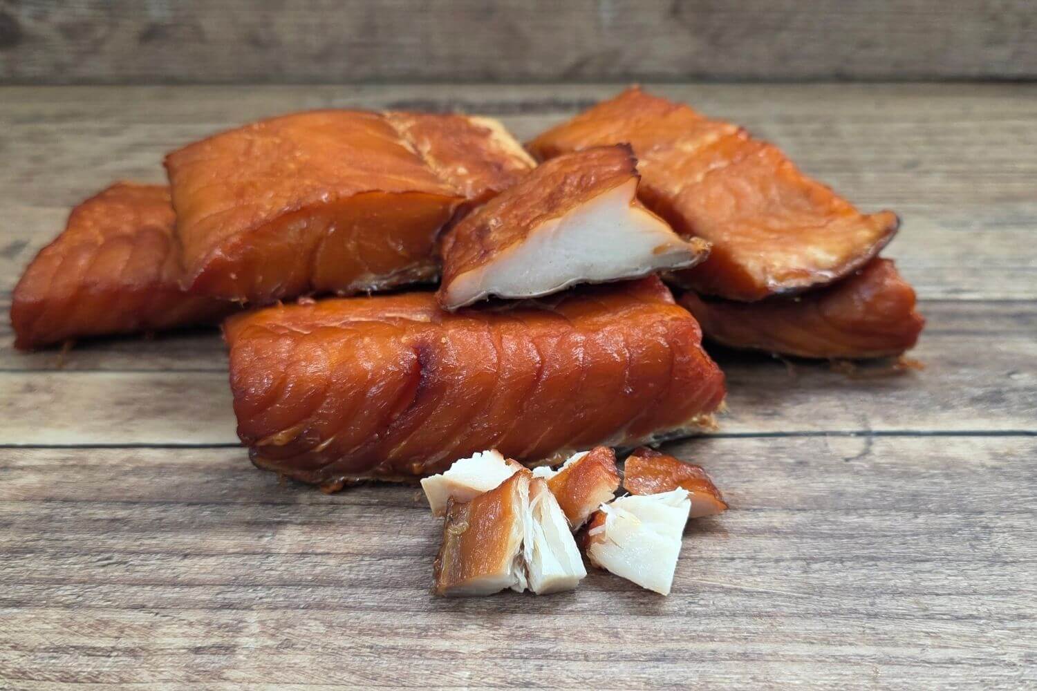 Hot-smoked wild Alaska lingcod portions with rich golden-brown color and firm white flakes displayed on a rustic wooden surface.