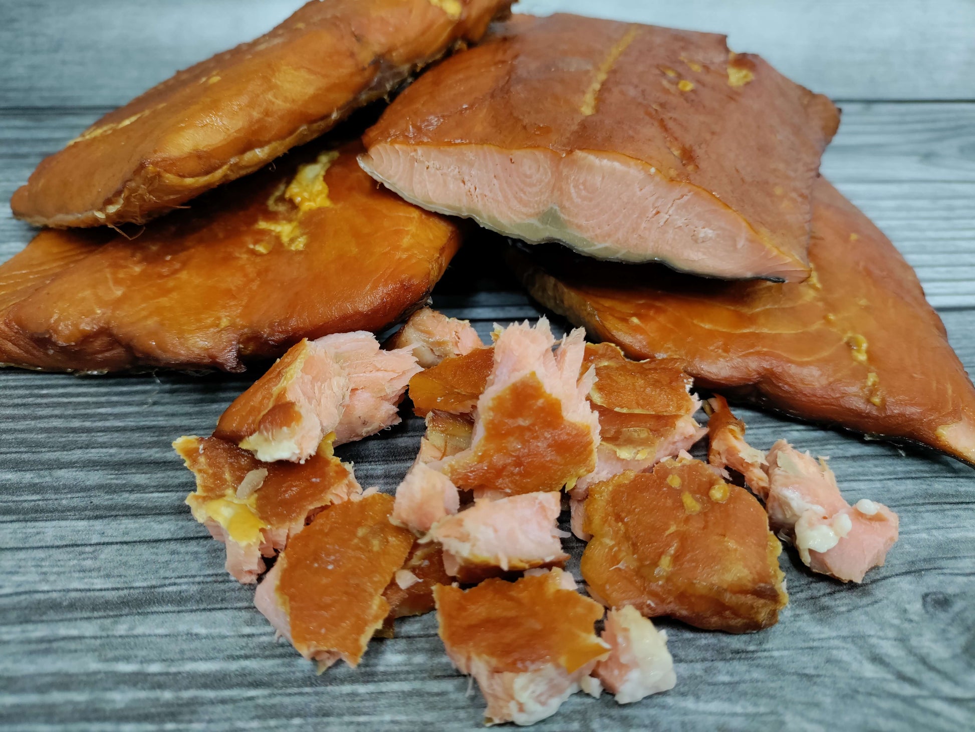 Smoked wild Alaskan coho salmon portions on a board with flaked pieces showing its firm, orange red texture.