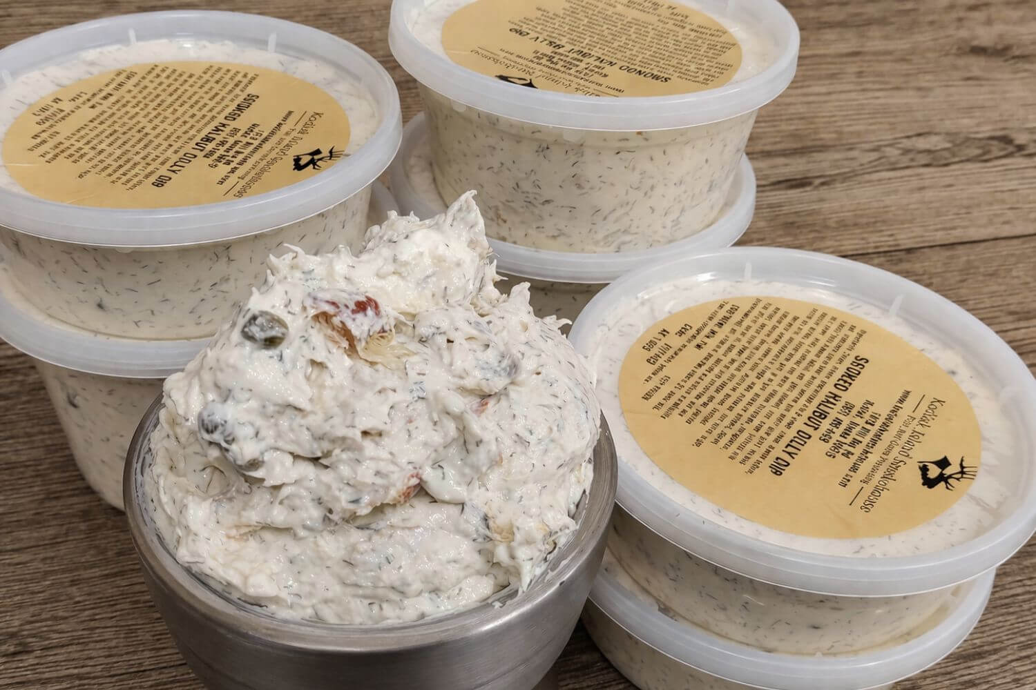 Containers of creamy smoked halibut dilly dip topped with dill and capers on a rustic wooden surface.