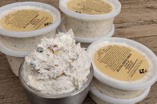 Containers of creamy smoked halibut dilly dip topped with dill and capers on a rustic wooden surface.