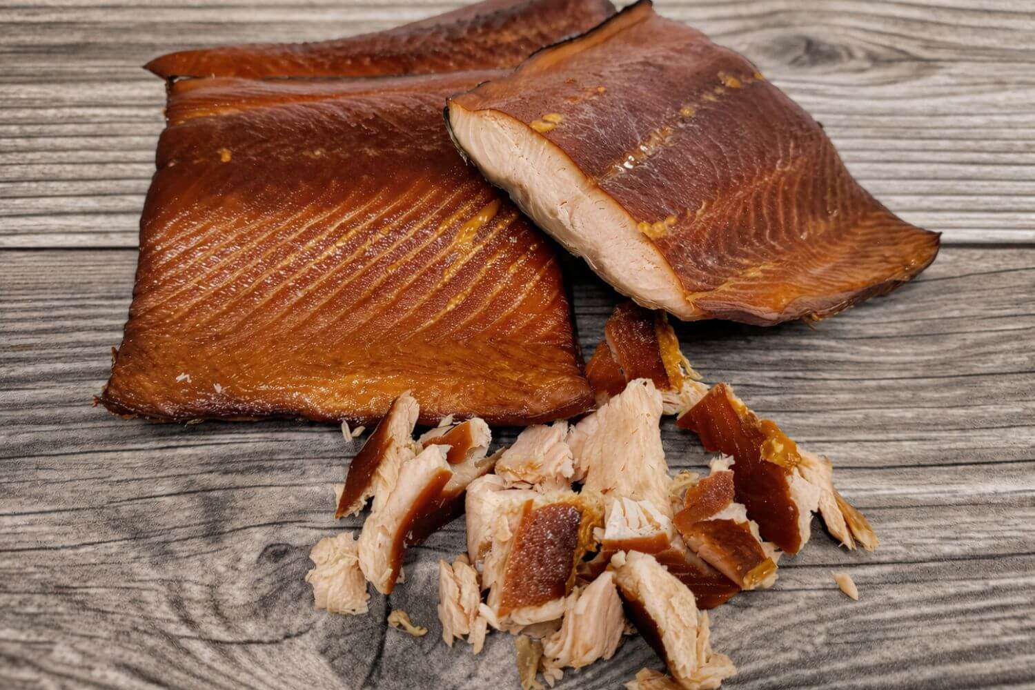 Portions and flakes of smoked wild Alaskan keta salmon on a wooden board.