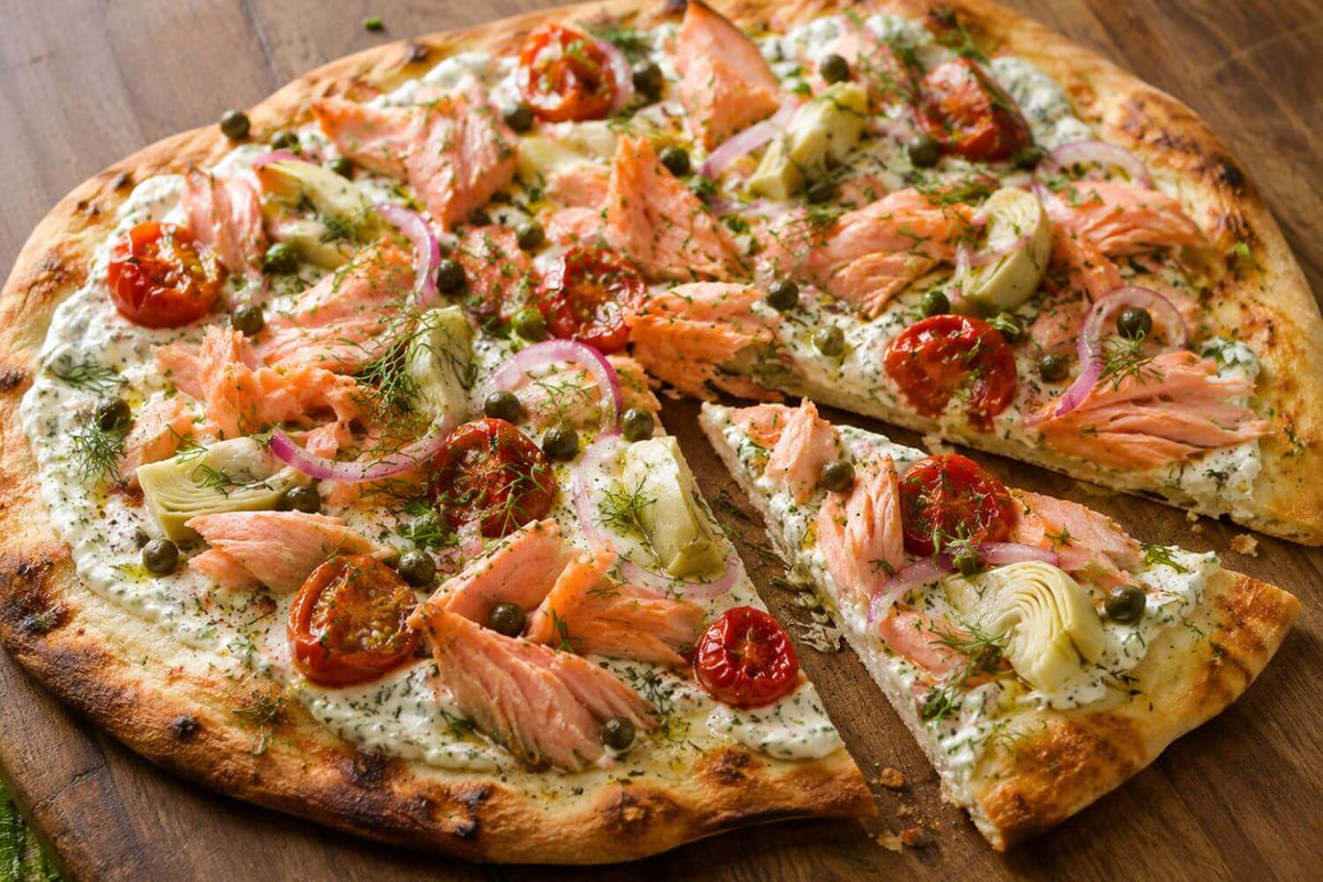 Smoked salmon pizza with herbed ricotta, roasted tomatoes, and fresh herbs on a rustic wood surface