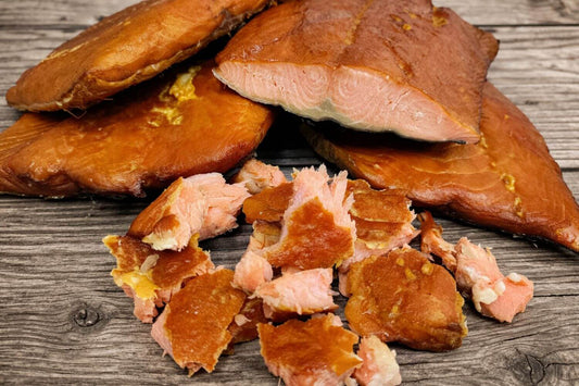 Smoked wild Alaskan coho salmon portions on a board with flaked pieces showing its firm, orange red texture.