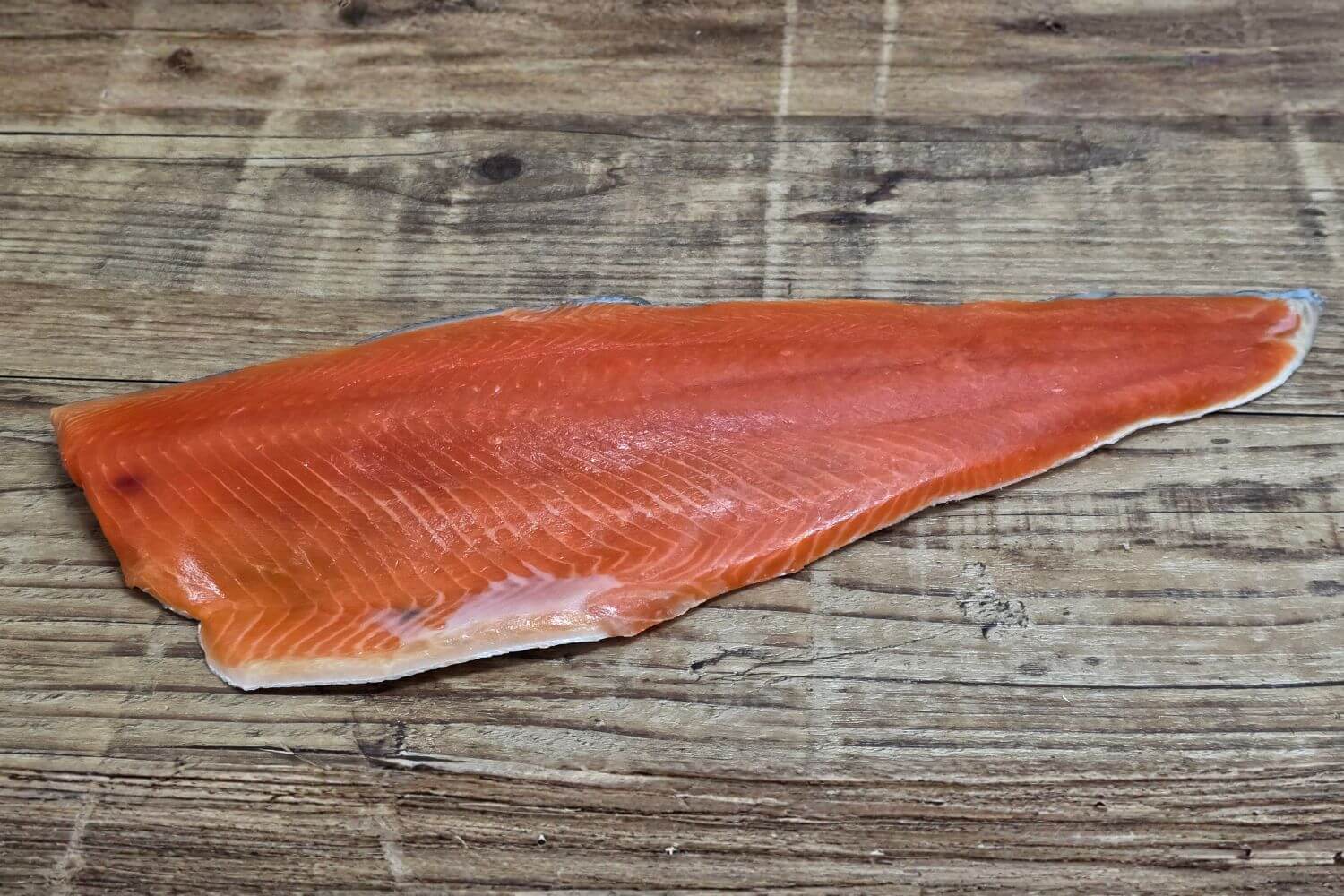 Full raw Wild Alaskan sockeye salmon fillet displayed on a rustic wooden background, showing its deep red color, fine grain, and natural sheen.