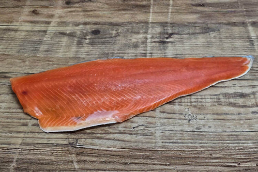 Full raw Wild Alaskan sockeye salmon fillet displayed on a rustic wooden background, showing its deep red color, fine grain, and natural sheen.