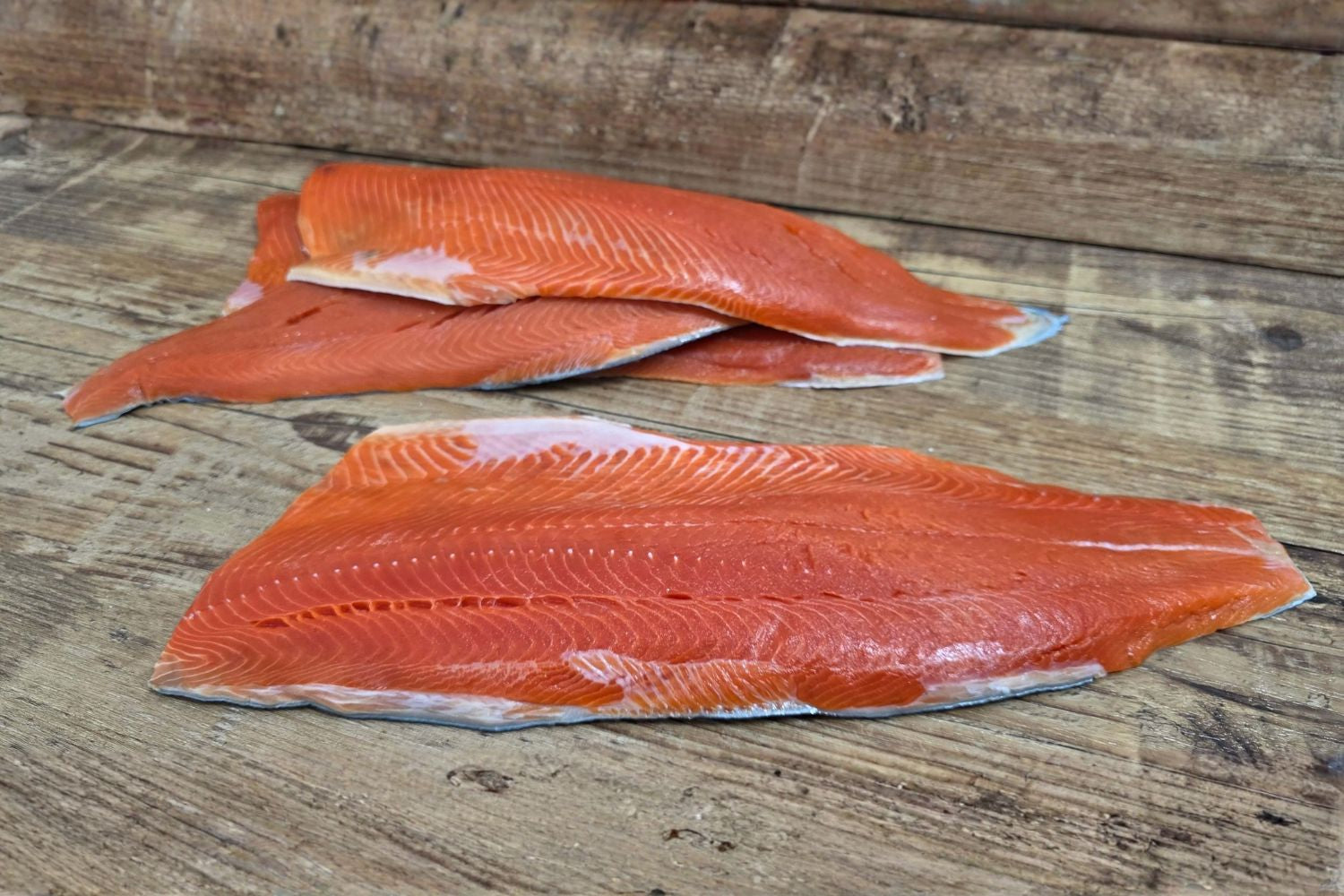 Raw Wild Alaskan sockeye salmon fillets on a rustic wood surface, showing the deep red color and clean cut lines.