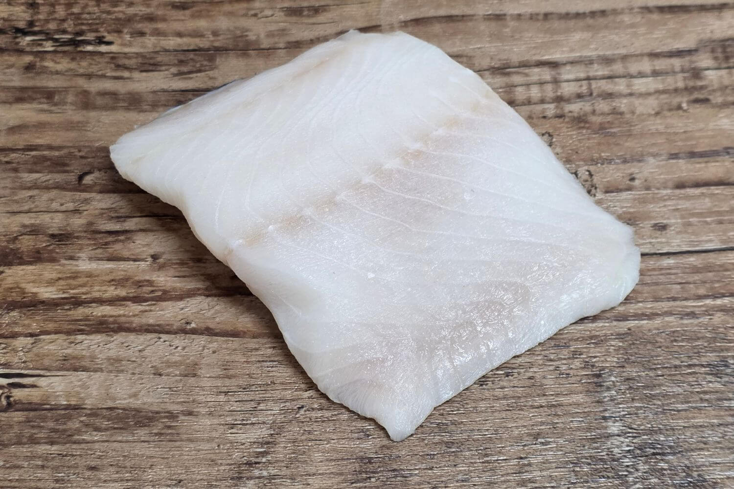 Raw Wild Alaskan black cod fillet on a rustic wood surface.