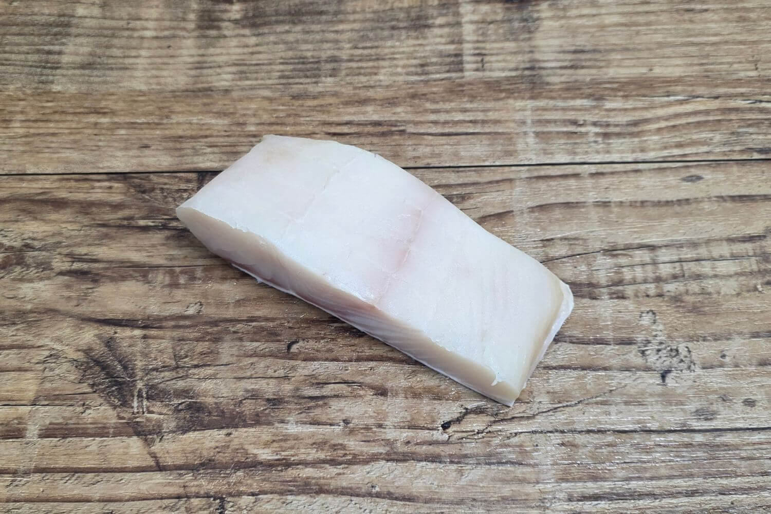 Single raw Wild Alaskan halibut fillet portion displayed on a rustic wooden background, showing its firm white flesh and natural grain.